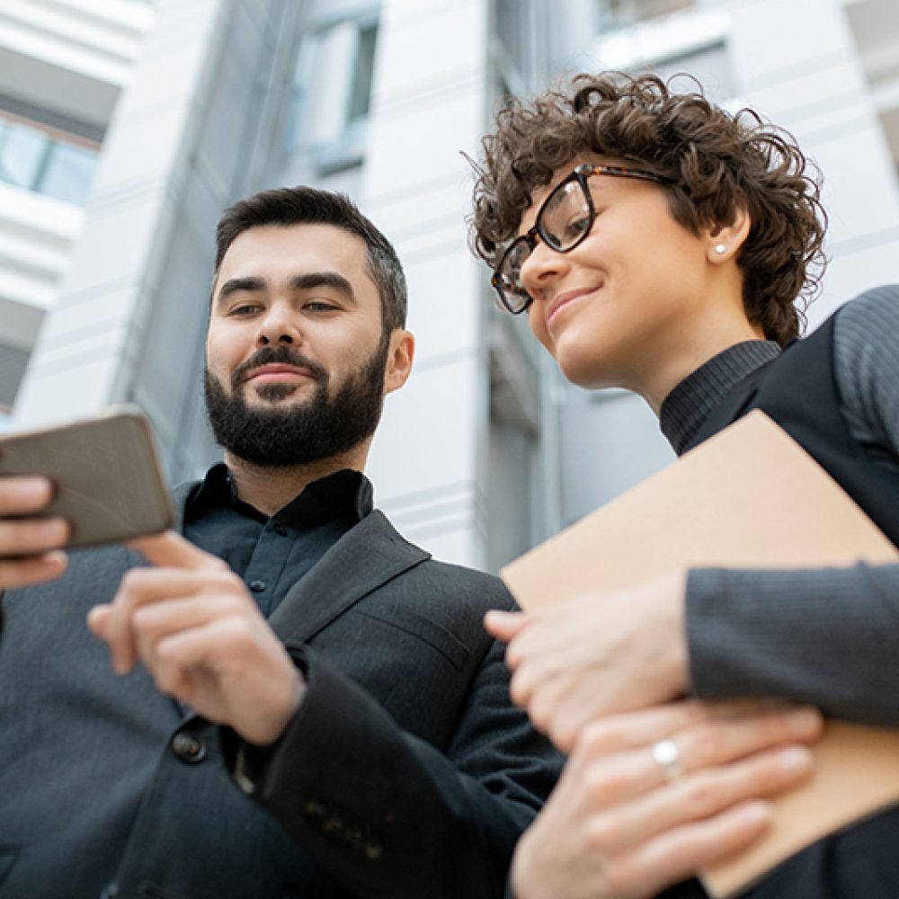 Below view of successful marketing specialists using smartphone while watching statistics on social media